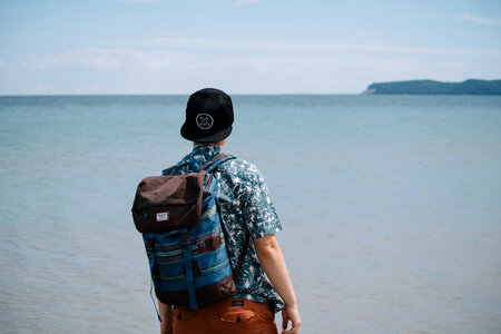 A Man with a Backpack Standing and Looking out Over a Calm Ocean photo