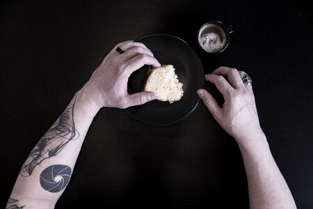 Close up of a Tattooed Man's Arms Eating Breakfast against Black Background photo