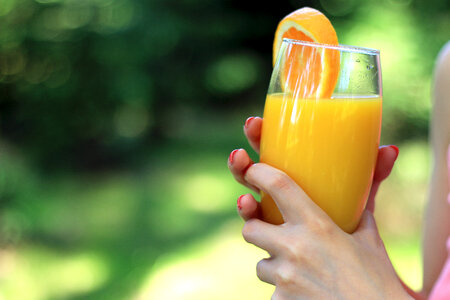 Glass of orange juice in the hands of woman in nature photo