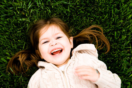 Portrait of a Laughing Little Girl Lying on Green Grass photo