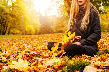 1 Young woman sitting on a fallen autumn leaves in a park photo