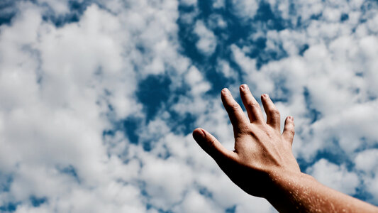 Human Hand against Blue Sky with Clouds photo