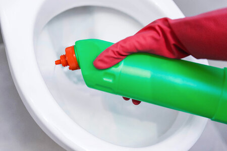 Woman hand with spray bottle cleaning a toilet bowl in a bathroom photo