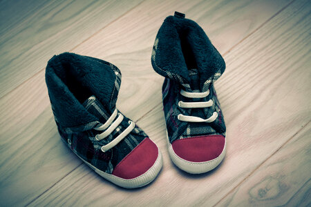 Pair of Cute Baby Sneakers over White Wooden Floor photo