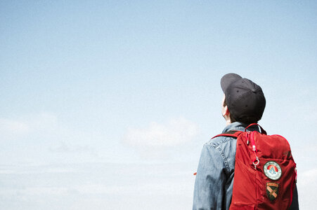 Young Man with Backpack Standing and Looking up at the Sky photo