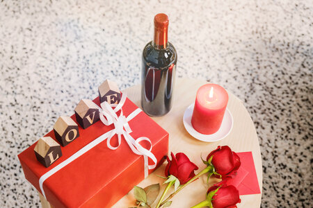 Wooden table with bottle of wine, roses and gift box photo
