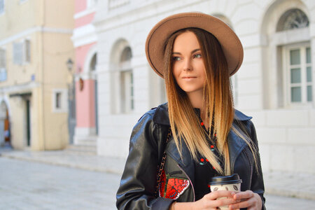 Beautiful Fashionable Woman in a Hat and Black Leather Jacket Holding Coffee photo