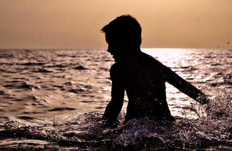 Child Silhouette Splashing Water over Sunset in the Sea photo