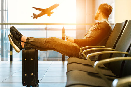 Man looking out window at flying airplane while waiting boarding on aircraft in airport lounge