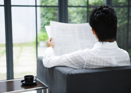 Man sitting on couch at home reading reading newspaper . photo