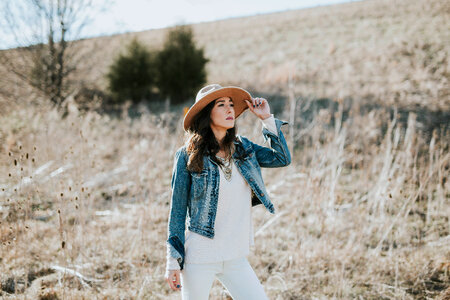 Young Woman in Hat and Denim Jacket Standing Outdoors photo