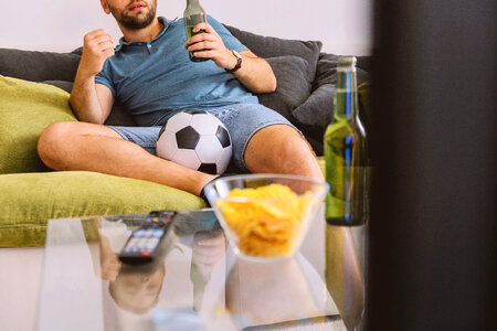 2 Young man watching football on TV and drinking beer at home photo