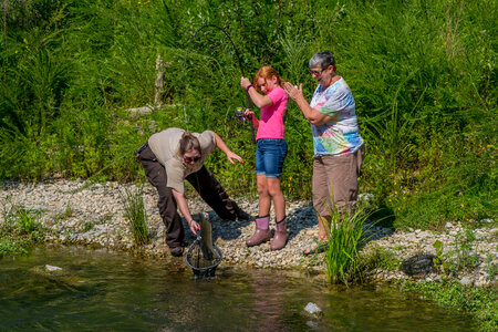Older woman fishing with young redheaded girl, FWS employee netting trout