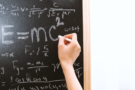 2 Female hand holding white chalk in front of a blackboard with Einstein formula. Education and school concept. photo