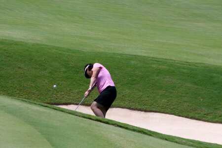 Young woman golfer chipping golf ball out of sand trap onto green photo