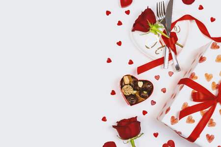 Valentine’s Day. Roses, hearts, gift box, plate with cutlery and box of chocolate on white background.