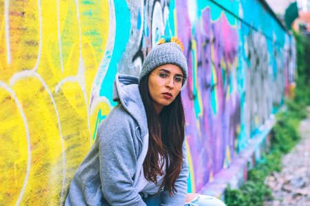 Young Woman Wearing Tracksuit and Glasses Sitting against Graffiti Wall photo