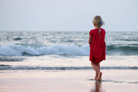 Beautiful Blonde Little Girl Dressed in a Red Dress Playing on the Beach photo
