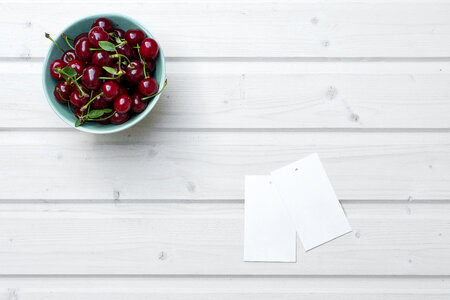 Empty Tag Cards and Cherries in Bowl on White Wooden Background photo