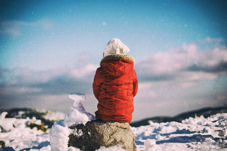 Child Sitting on the Rock when It Is Snowing photo