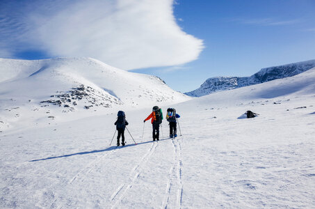 Three People Walking over Snowy Valley with Backpacks photo