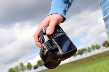 Detail of hand that holds DSLR camera in landscape photo
