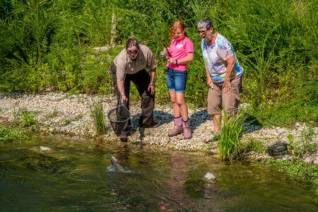Older woman fishing with young redheaded girl, FWS employee netting trout-5