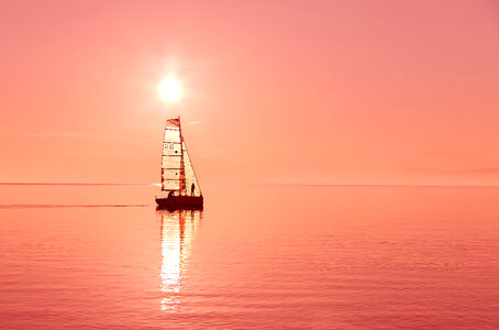 Boat sailing under the red sun on a lake photo