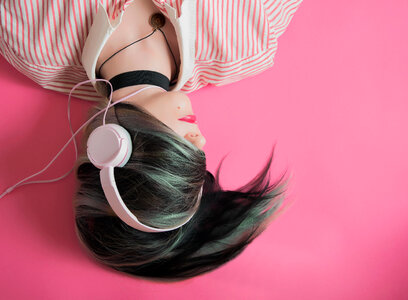 Young Girl Listen to Music Lying on Pink Background photo