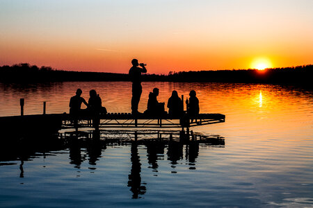 Silhouette of Group of Friends Sitting and Drinking on a Lake Pier at Sunset photo
