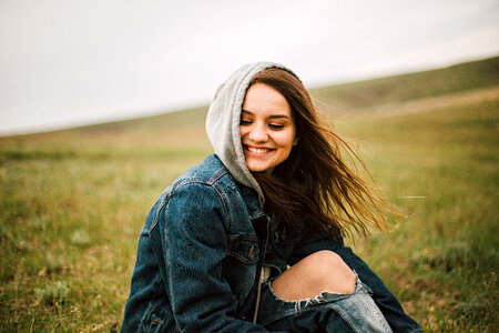 Smiling Long-hair Girl in a Hood Sitting in the Meadow photo