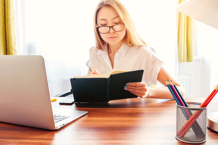 Young woman make notes in her diary. Laptop and pencils on a table in front of her photo