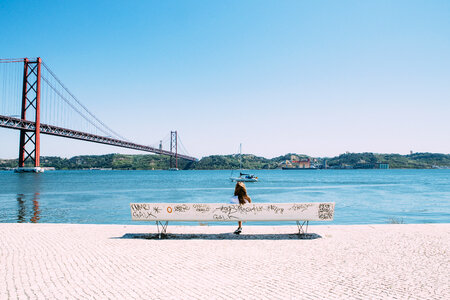 Young Girl sitting on the Bench near the 25th of April Bridge, Lisbon photo