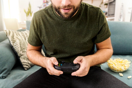 Close up of man eats popcorn, holding joy stick and playing video games on tv at vacation, sits at home on the couch. photo