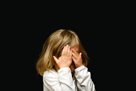 Little Girl Covering Her Face with her Hands on Black Background photo