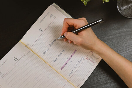 The woman’s hand holds a pencil and writes a plan into a diary in the office