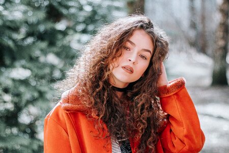 A young woman with long curly hair wears an orange winter jacket photo