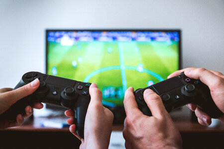 Hands holding the game controller while playing game on TV