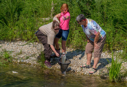Older woman fishing with young redheaded girl, FWS employee netting trout-1