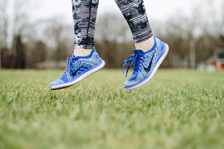 Closeup of Female Legs Wearing Blue Sneakers Jumping on the Grass Outdoors photo