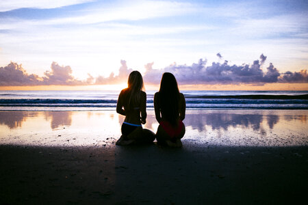 Two Young Woman Sitting on the Beach during Sunset photo