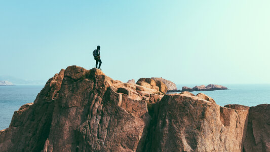 Young Man with Backpack Is Standing on Cliff's Edge and Looking photo