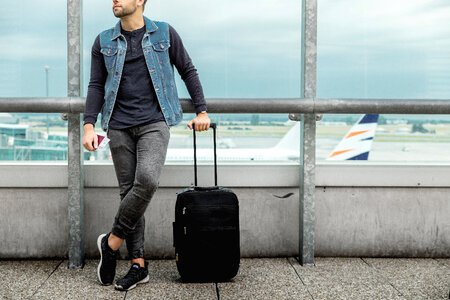 Male tourist is standing outdoor in airport with a luggage photo
