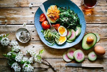 Top View of Healthy Salad Bowl with Eggs, Tomatoes, Avocado and other Vegetables on Wooden Table photo