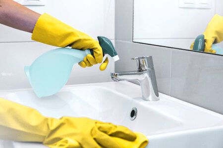 Woman doing chores in bathroom at home. Cleaning sink and faucet with spray detergent photo