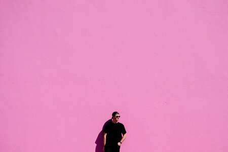 Man in Black T-shirt, Cap andSunglasses Leaning on Pink Wall photo