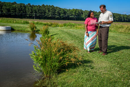 FWS Staffer shows young woman in dress a field guide by wetland