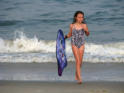 Young girl walking from the water carrying her boogie board photo