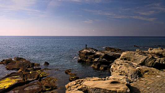 Person fishing on the cliffs near the ocean photo