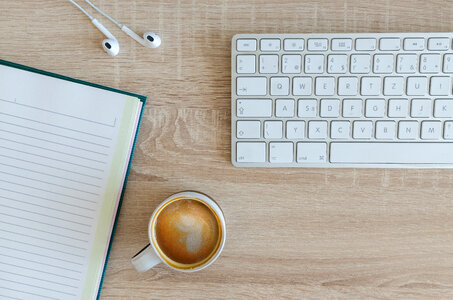 Flat Lay Photo of Wooden Desk with Keyboard, Notebook, Earphones and Coffee